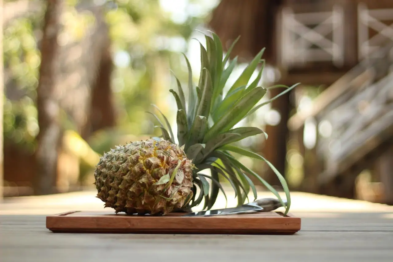 A vibrant pineapple resting on a chopping board with a knife, captured outdoors in natural light.